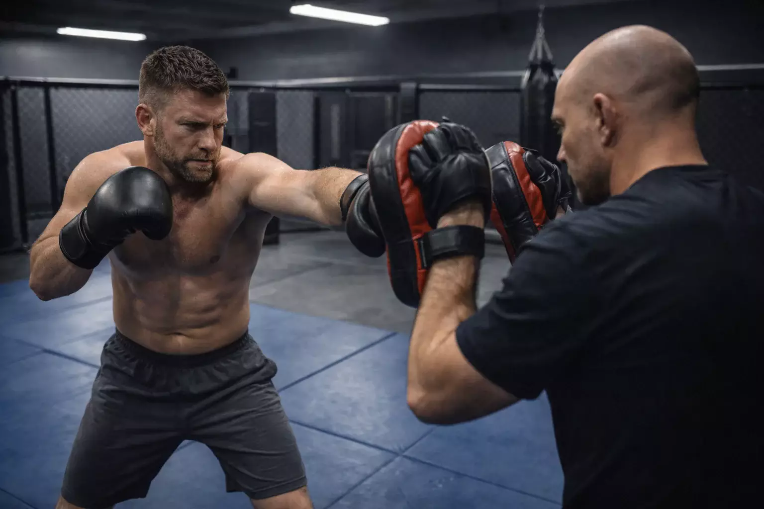 Peleador de MMA entrenando en un gimnasio con su entrenador sujetando paos